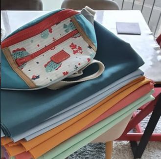 Sac Camper posé sur une pile de tissus colorés